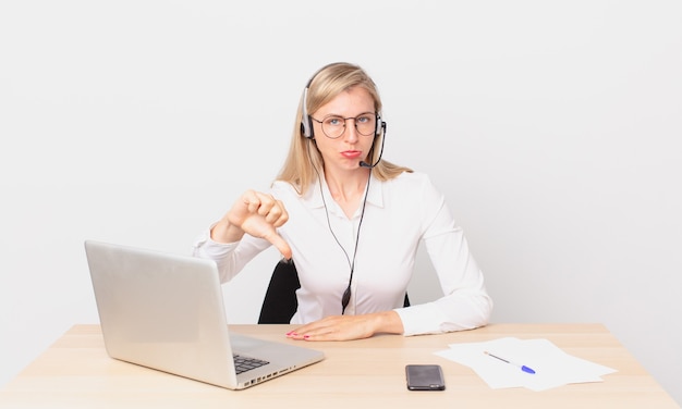 Bionda bella donna giovane donna bionda che si sente arrabbiata, mostra i pollici in giù e lavora con un laptop