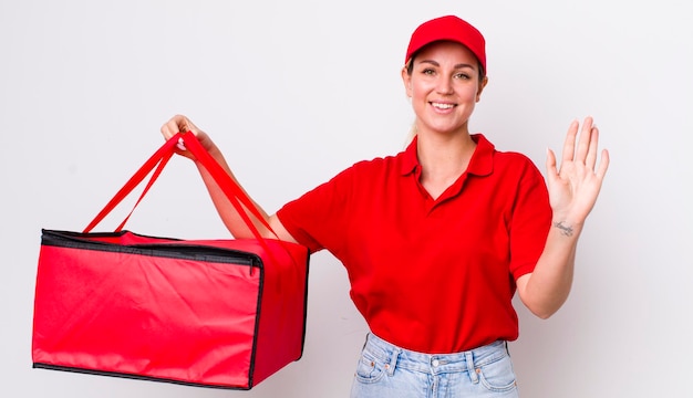 Bionda bella donna sorridente felicemente agitando la mano dandoti il benvenuto e salutandoti concetto di consegna della pizza