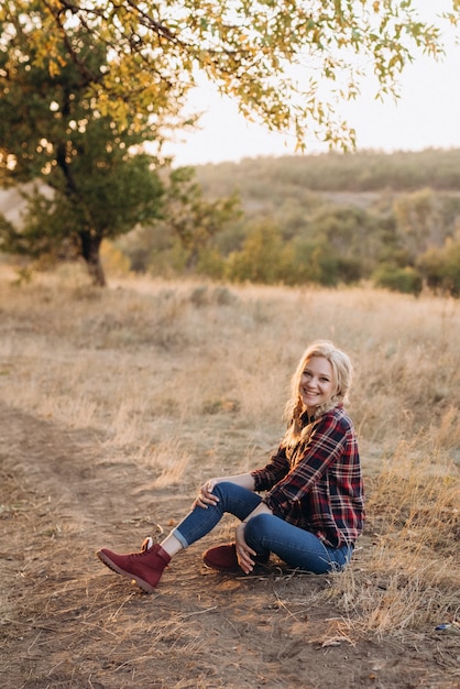 Bionda con le trecce in camicia, jeans, scarpe rosse che sorride al tramonto