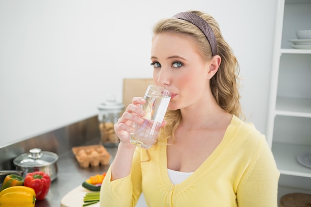 Bionda contenta che beve un bicchiere d&#39;acqua