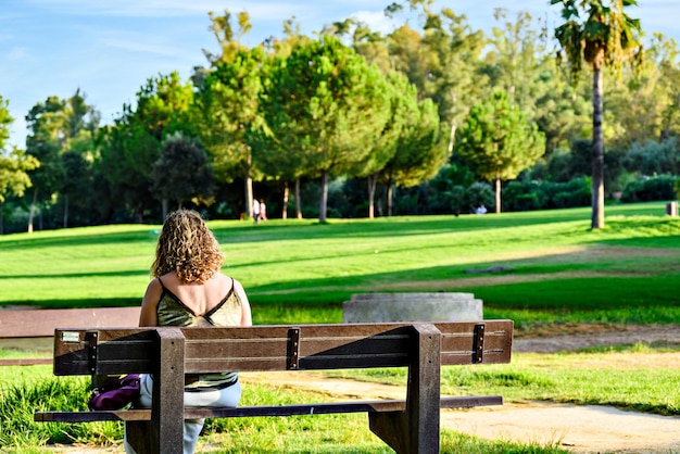 Bionda dai capelli ricci donna seduta su una panchina nel parco la Retama ad Alcala de Guadaira, Siviglia Spagna.