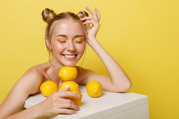 Bionda di modello con i limoni che sorridono su una priorità bassa gialla