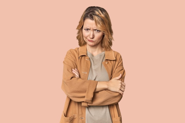 Bionda donna caucasica di mezza età in studio con la faccia accigliata di dispiacere e le braccia incrociate.