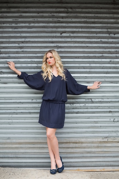 Bionda elegante seria che porta vestito di classe che posa all&#39;aperto