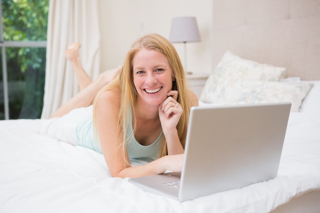 Bionda felice che per mezzo del computer portatile sul letto