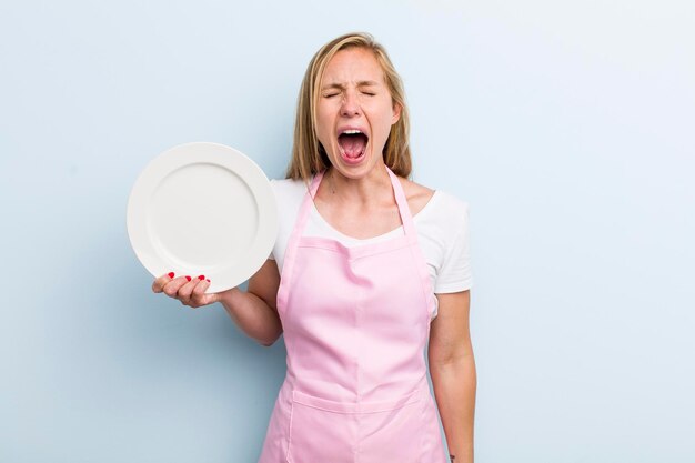 Bionda giovane donna adulta che tiene un concetto di chef piatto vuoto