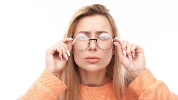 Bionda giovane donna che indossa gli occhiali strizzando gli occhi mentre guarda la fotocamera isolata su sfondo bianco Concetto di problemi di visione