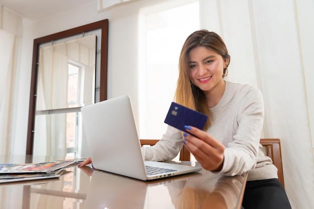 bionda giovane donna sorridente davanti al computer portatile guardando la sua carta di credito prima dello shopping online