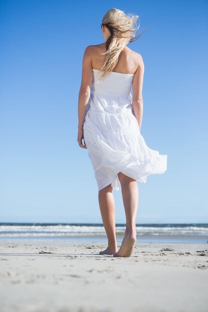 Bionda in abito bianco che passeggia sulla spiaggia