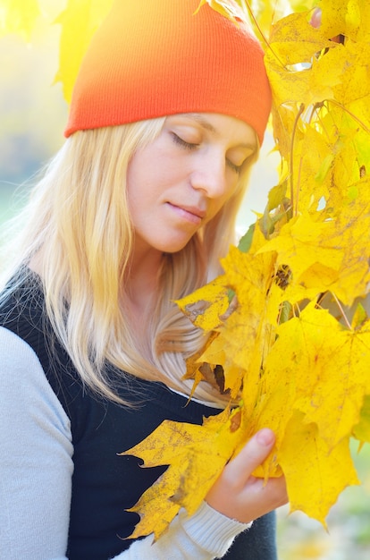 Bionda in un cappello arancione per godersi la natura nel parco d'autunno