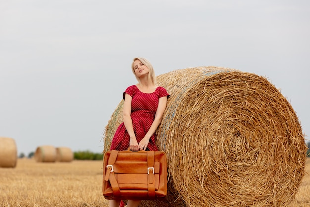 Bionda in un vestito rosso con la valigia in un campo di grano prima della pioggia