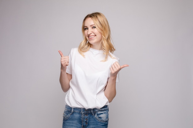 Bionda positiva in camicia bianca e jeans che mostrano i pollici in su