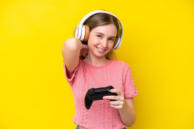 Bionda ragazza inglese che gioca con un controller per videogiochi isolato su sfondo giallo ridendo