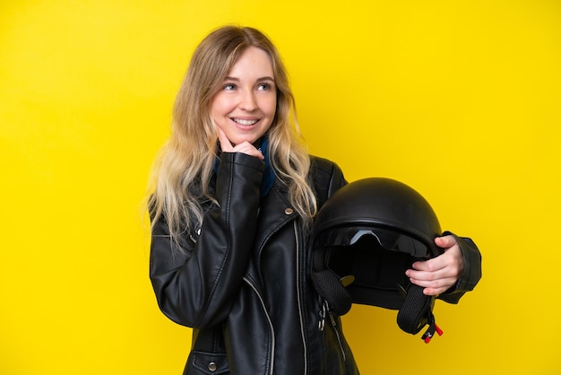 Bionda ragazza inglese con un casco da motociclista isolato su sfondo giallo che pensa un'idea mentre cerca