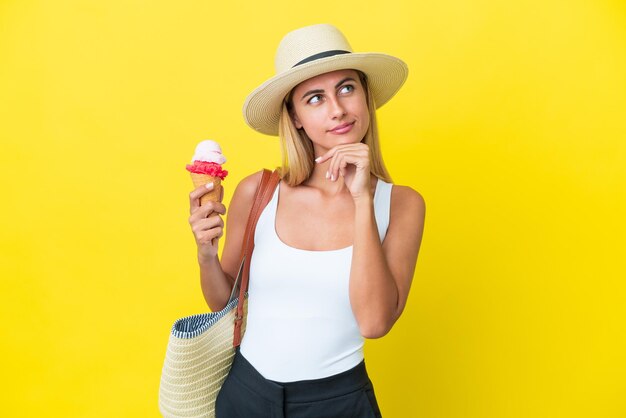 Bionda ragazza uruguaiana in estate con gelato isolato su sfondo giallo con dubbi