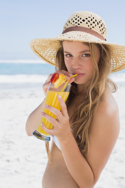 Bionda sorridente graziosa in bikini che tiene cocktail sulla spiaggia