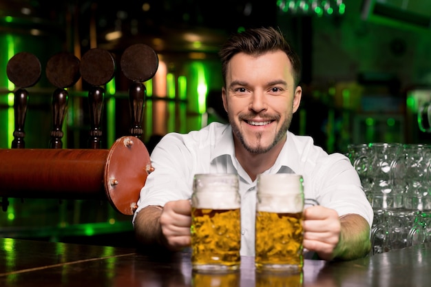 Birra appena spillata. Bel barista sorridente che allunga boccali di birra e sorride