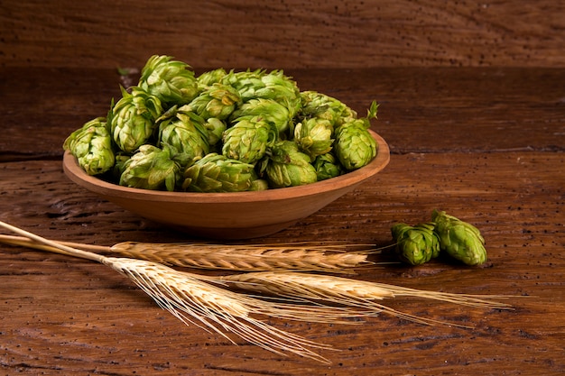 Birra che fa gli ingredienti Coni di luppolo in orecchie di legno della ciotola e del grano su fondo di legno. Concetto di birrificio di birra.