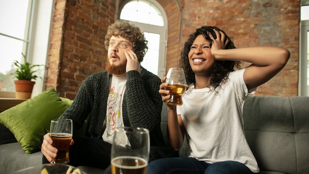 Birra. Coppia eccitata, amici che guardano la partita sportiva, il campionato a casa. Amici multietnici, fan che tifano per la squadra nazionale preferita di basket, tennis, calcio, hockey. Concetto di emozioni.