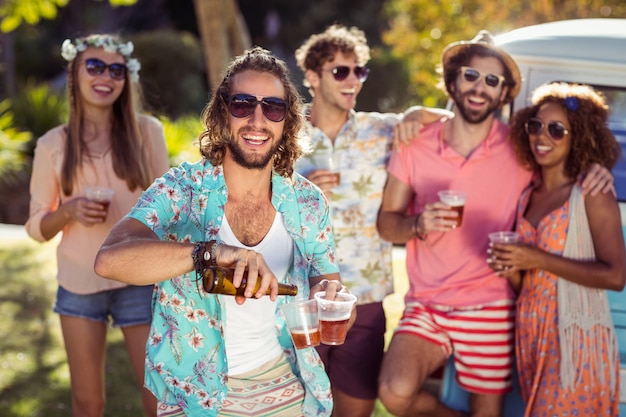 Birra di versamento dell'uomo felice in un vetro mentre i suoi amici che stanno nel fondo