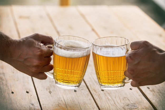 Birra in bicchieri grandi e luce di vetro dorata con schiuma e mani di close-up amici