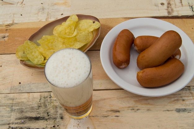 Birra in un bicchiere con spuma salsicce chip su tavole nel giardino tema Oktoberfest