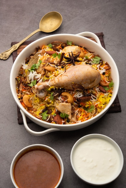 Biryani di pollo piccante in stile ristorante servito con Raita e Salan, cibo popolare indiano o pakistano non vegetariano?