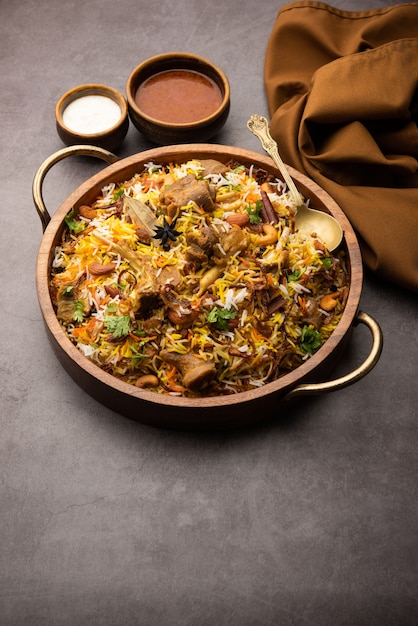 Biryani indiano di montone preparato con riso basmati servito con salsa di yogurt su sfondo lunatico, messa a fuoco selettiva