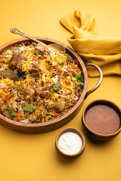 Biryani indiano di montone preparato con riso basmati servito con salsa di yogurt su sfondo lunatico, messa a fuoco selettiva