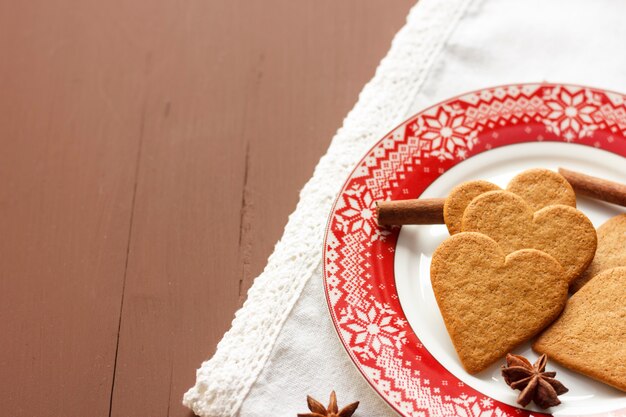 Biscotti a forma di cuore di pan di zenzero con bastoncini di cannella e stelle di anice su un piatto rosso