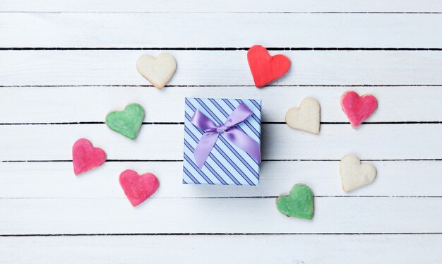 Biscotti a forma di cuore e confezione regalo su fondo di legno bianco