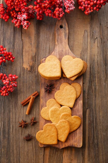 Biscotti a forma di cuore sul tagliere con bacche di cenere e cannella su fondo di legno