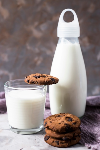 Biscotti al cioccolato accanto a una bottiglia di vetro e un bicchiere di latte su un tavolo grigio