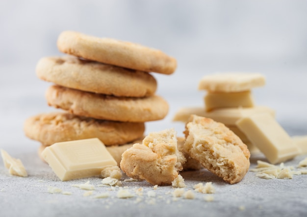 Biscotti al cioccolato bianco con blocchi di cioccolato e riccioli sul tavolo luminoso.