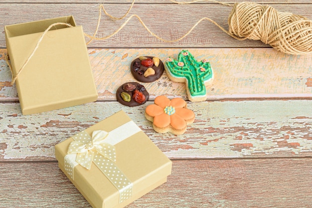 Biscotti al cioccolato con noci ea forma di fiore e cactus, accanto a piccole scatole regalo e un rotolo di spago.