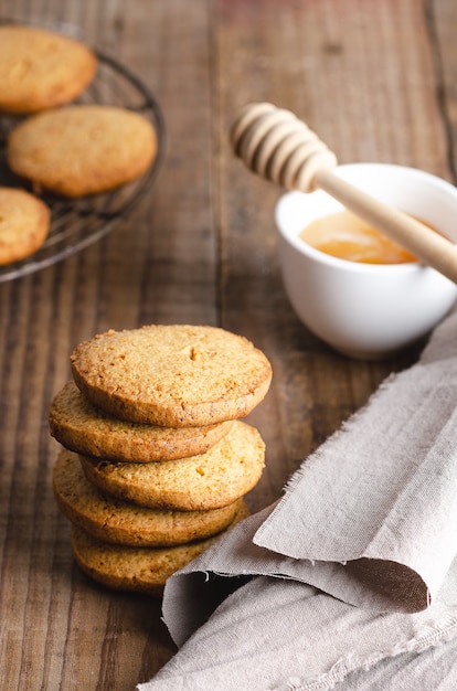 Biscotti al miele con un tovagliolo beige e una ciotola con miele e un mestolo di miele su un tavolo di legno