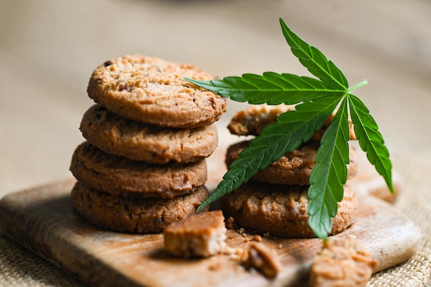 Biscotti alimentari alla cannabis con foglie di cannabis erba di marijuana su fondo di legno, delizioso biscotto da dessert dolce con pianta di foglie di canapa THC CBD erbe spuntino alimentare e concetto medico