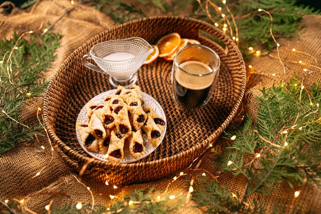 Biscotti alla marmellata con caffè e latte su cesto con ghirlanda e rami di abete