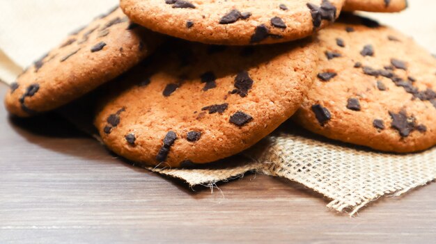 Biscotti americani al cioccolato su un tavolo di legno marrone e su un primo piano di un tovagliolo di lino. Tradizionale impasto tondo croccante con gocce di cioccolato. Forno. Dessert delizioso, pasticcini. Natura morta rurale.