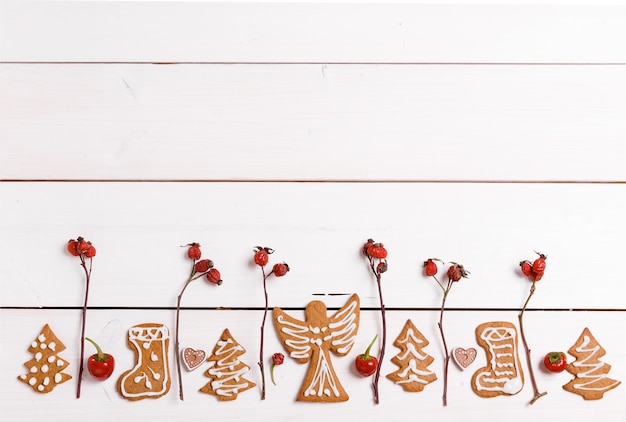 Biscotti casalinghi del pan di zenzero di Natale e bacche rosse del cinorrodo, sulla tavola di legno bianca. Bandiera di Natale. T