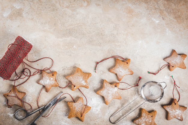 Biscotti casalinghi della stella del pan di zenzero di Natale con la polvere dello zucchero, corda verde-rossa della decorazione sulla pietra leggera, vista superiore, copyspace