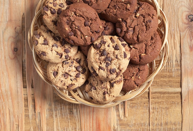 Biscotti con cioccolato e noci in piatto di vimini su fondo di legno vecchio, vista dall'alto