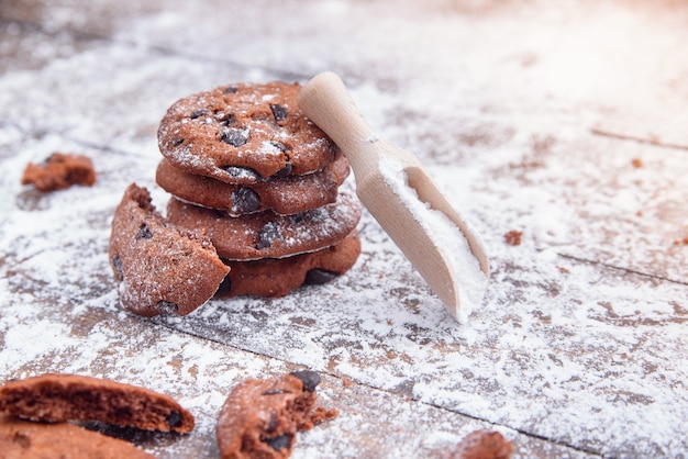 Biscotti con fette di cioccolato cosparsi di zucchero a velo e un misurino di legno. Pasticceria fresca su legno.