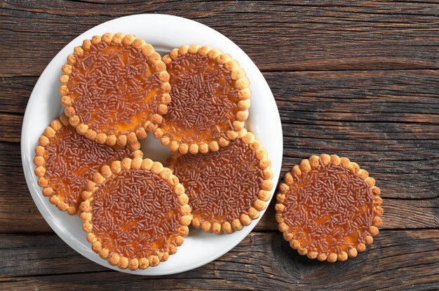 Biscotti cosparsi di cioccolato e marmellata di arance nel piatto su fondo di legno scuro vista dall'alto