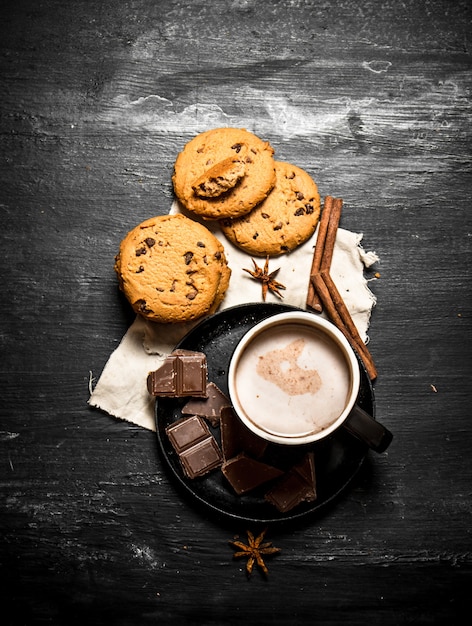 Biscotti d'avena con pezzetti di cioccolato e bevanda al cacao. Su un tavolo di legno nero.