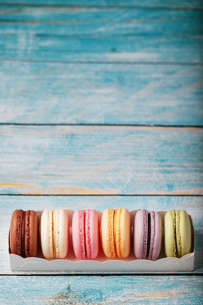 Biscotti dei maccheroni dei colori differenti in una scatola su un fondo di legno blu e vecchio di colore blu.