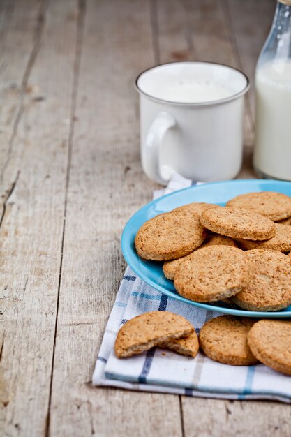 Biscotti di avena appena sfornati sul piatto in ceramica blu sul tovagliolo di lino e tazza di latte.