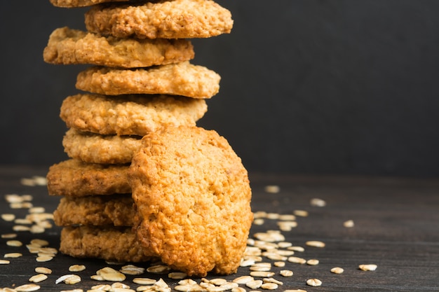 Biscotti di farina d'avena casalinghi con l'avena asciutta sulla tavola di legno, foto scura