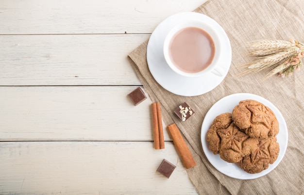 Biscotti di farina d'avena casalinghi con una tazza di cacao su un fondo di legno bianco. vista dall'alto, copia spazio.