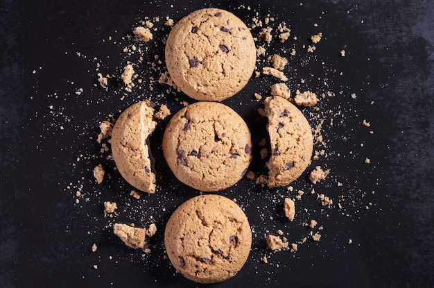 Biscotti di farina d'avena con cioccolato, interi, rotti e briciole sullo sfondo del vecchio metallo nero, vista dall'alto